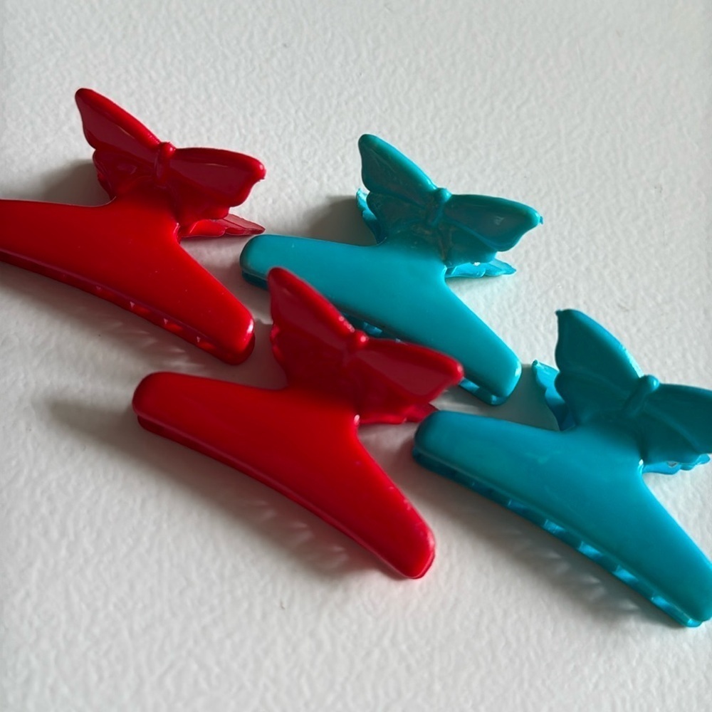 Red and teal moulded plastic mini butterfly claw clips from the 1990s laid on a white surface